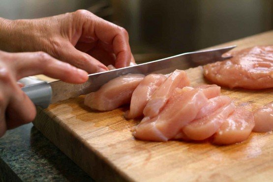 Un cuiner talla pollastre damunt una fusta